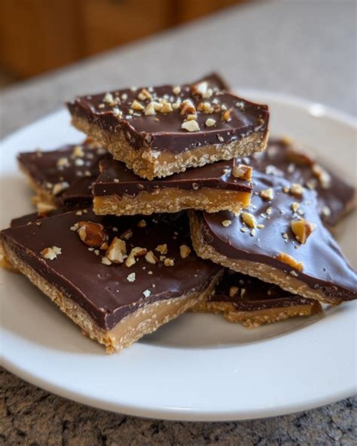 Graham cracker toffee topped with chopped almonds on a white plate next to a red and white striped napkin.