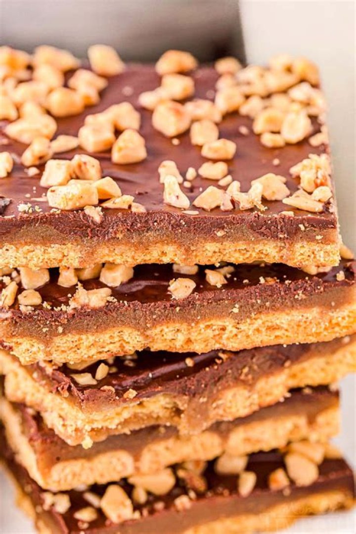 Stack of graham cracker toffee on a white plate next to a red and white striped napkin.